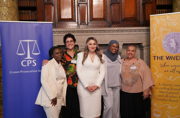 Group of five women standing together, smiling, in a formal setting with banners behind them.