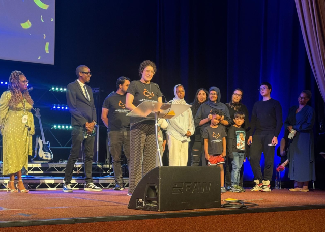 Group of people on stage, some holding awards, at an event, with a microphone in front.