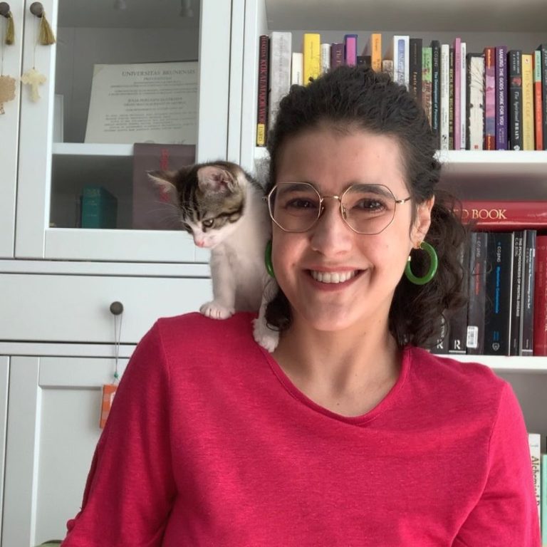 Smiling woman with curly hair and glasses, a kitten sitting on her shoulder.