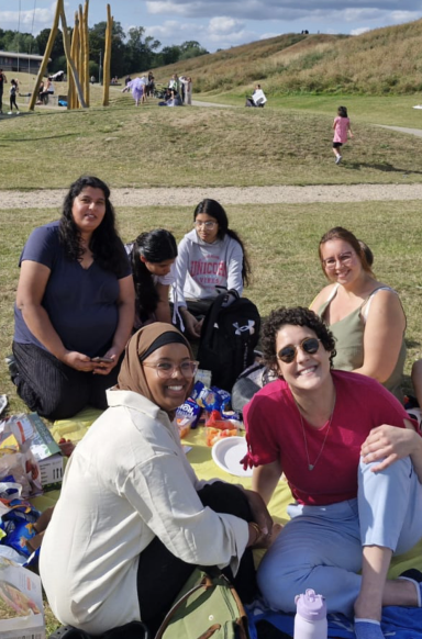 A group of women sitting on a picnic blanket in a park, enjoying food and each other's company.